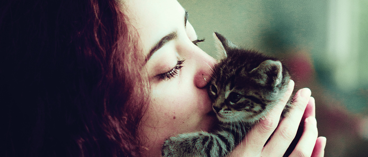 woman with brown hair kissing a kitten